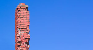 A damaged brick chimney against a blue sky