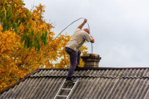 Male from chimney cleaning company sweeping a chimney